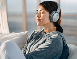 A woman sits with her eyes closed, listening to headphones.