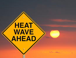 A road sign in front of a sunset. Sign reads: "Heat wave ahead."
