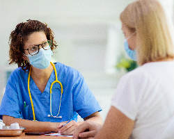 Health care provider takes notes while she talks with a patient (both wearing masks).