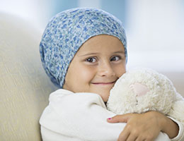 A child battling cancer smiles while hugging a stuffed animal. 