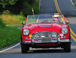 A man in a Panama hat drives a red convertible.