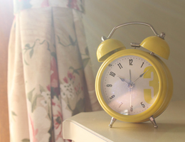 A vintage yellow alarm clock sits on a bedside table.