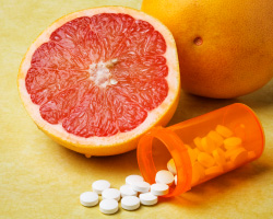 Half of a grapefruit next to a bottle of pills. 