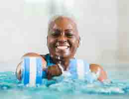 Older woman in pool smiling, doing water aerobics.