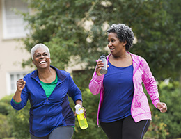  Two women carry water bottles and walk down a leafy street