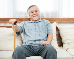 A man with a cane sits on cushions on a wooden bench
