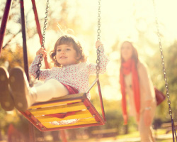 A toddler on a swing with a woman in the background.