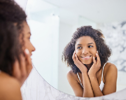 A woman looks in the mirror while touching her face.