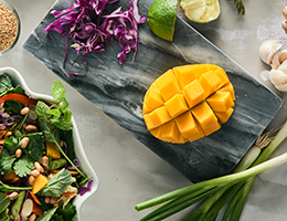 A mango on a cutting board with salad ingredients.