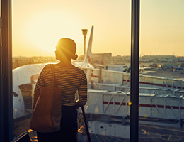 A woman standing in an airport and looking out a window at an airplane.