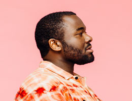 A profile of a man in an orange shirt on a pink background. 