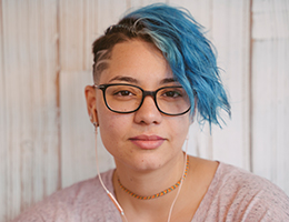 A teenager with blue hair and glasses.