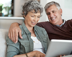 An older woman looks at a laptop as an older man puts his arm around her.