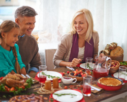 A happy man, woman, girl and boy sit at a table laden with Thanksgiving food. 